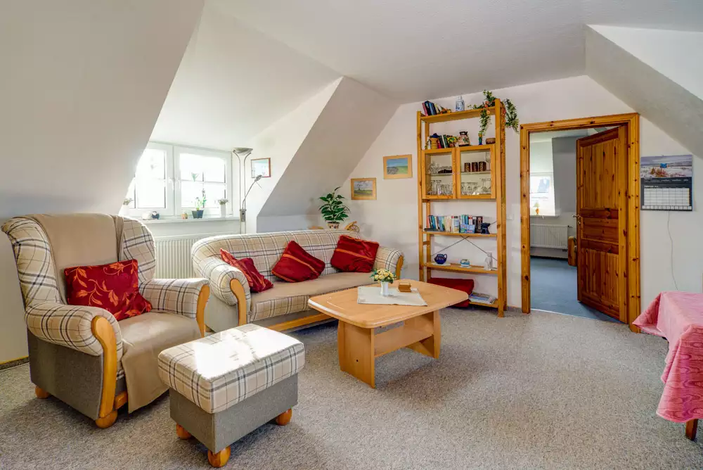 Gemütliche Couchecke mit Zweisitzer, Ohrensessel und Bücherregal im Wohnzimmer der Ferienwohnung Deichgraf