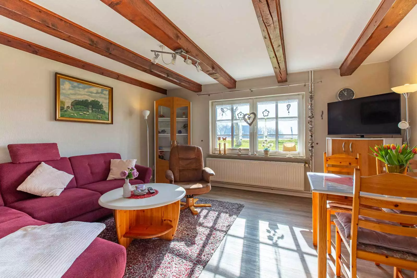 Wohnzimmer der Ferienwohnung Höck Hallig mit Couchecke, Essplatz und Blick aus dem Fenster ins Grüne