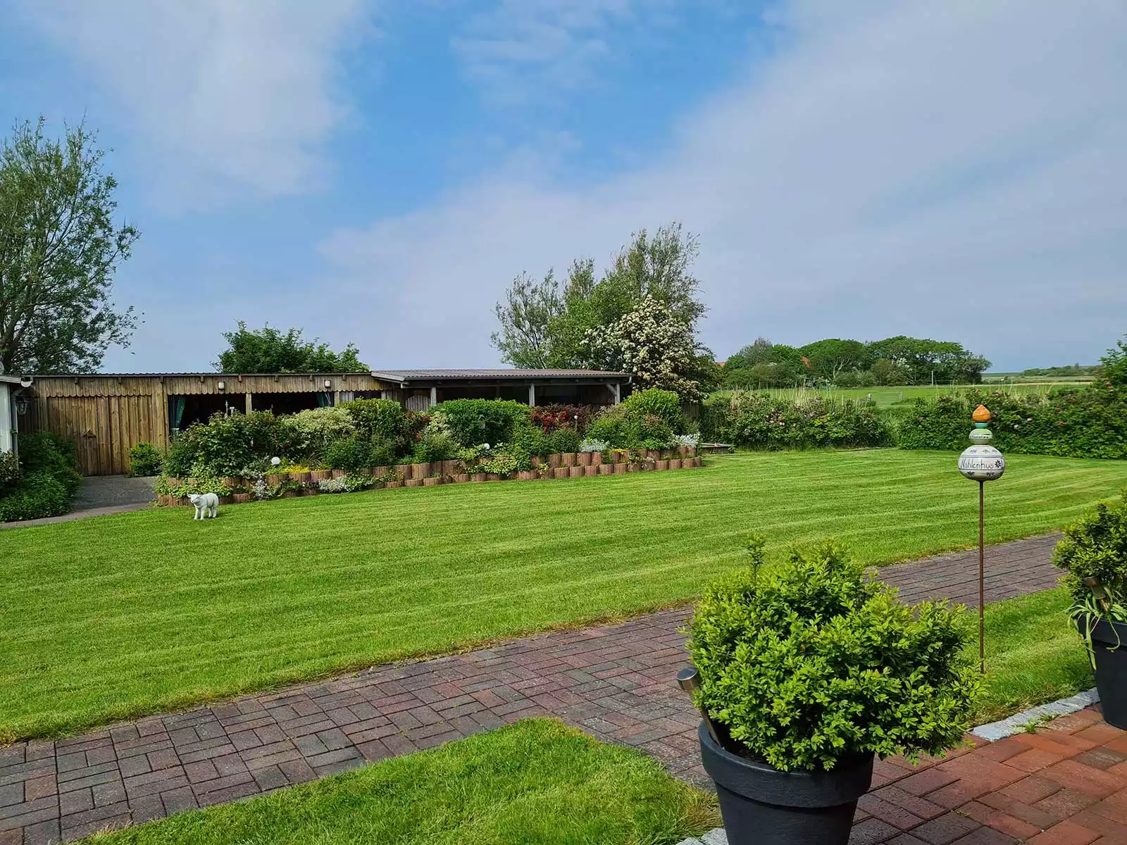Blick aus der Ferienwohnung Schimmelreiter in den blühenden Garten mit Sträuchern und freiem, unbebautem Land auf Pellworm