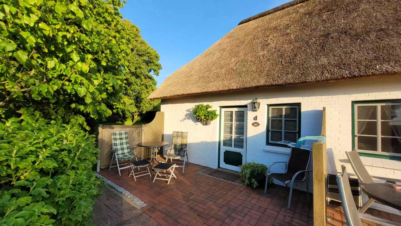 Terrasse der Ferienwohnung Schimmelreiter mit Gartenmöbeln in der Abendsonne, umgeben von viel Natur auf Pellworm