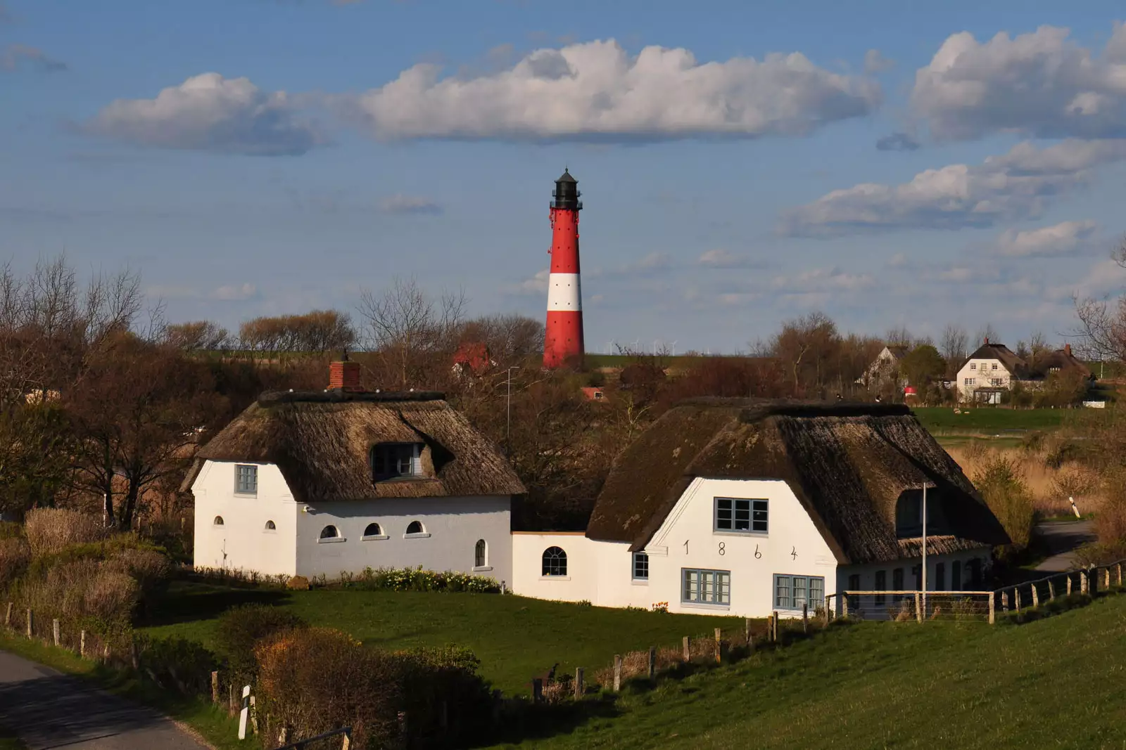Blick vom Deich über Reetdachhäuser zum Leuchtturm auf Pellworm in der Sonne