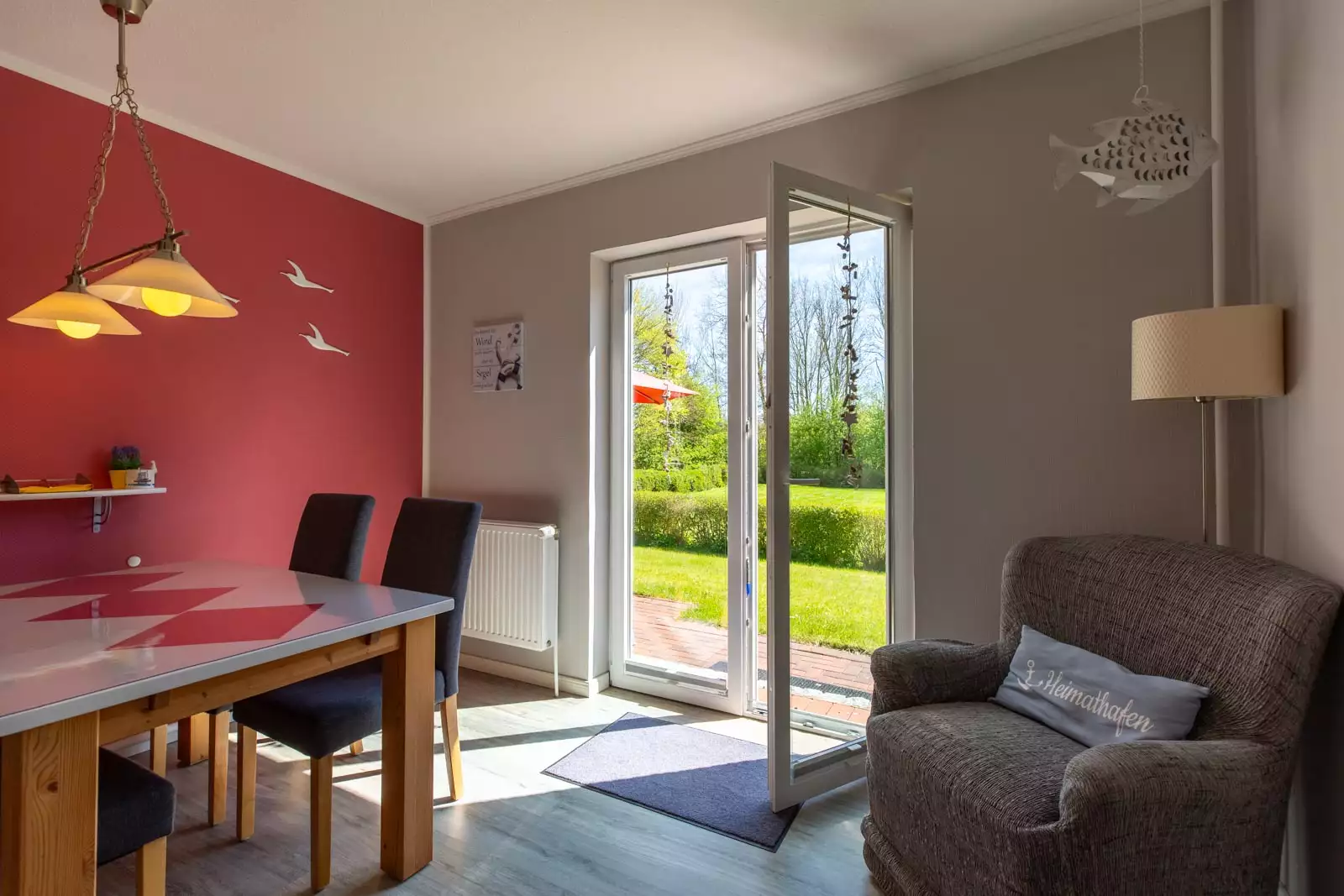 Esszimmer im offenen Wohnraum der Ferienwohnung Heimathafen mit Esstisch, Stühlen und Lesesessel neben der Terrassentür