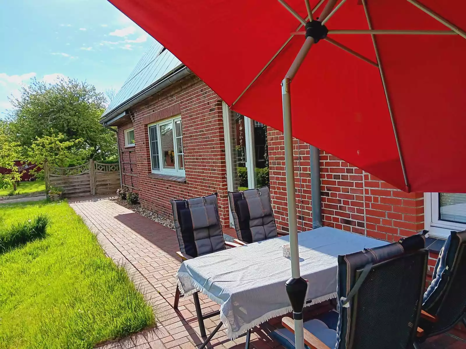 Terrasse der Ferienwohnung Heimathafen mit Gartenmöbeln, Tisch, Stühlen und aufgespanntem Sonnenschirm