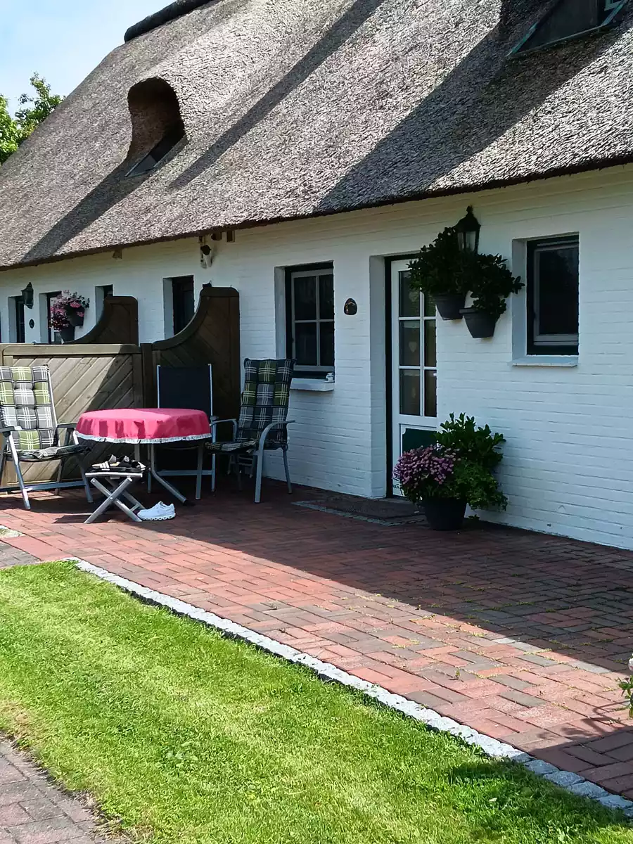 Terrasse der Ferienwohnung Springflot unter Reetdach mit Gartenmöbeln und blühenden Blumenkübeln