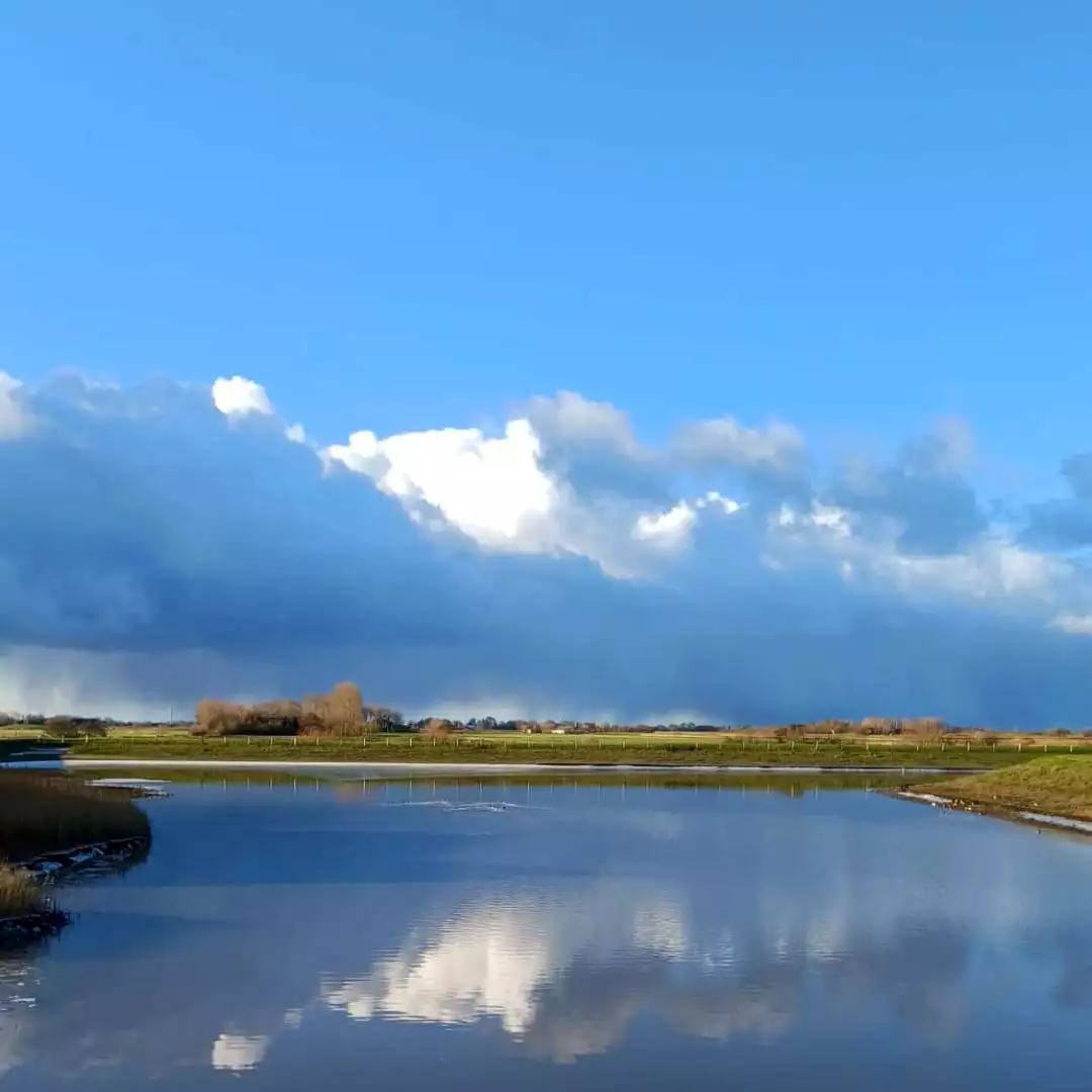 Siel in Hafennähe auf Pellworm mit spiegelnden Wolken im Wasser und Blick über die Insel.